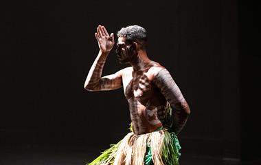 A man in a grass skirt with white body paint performing on stage.