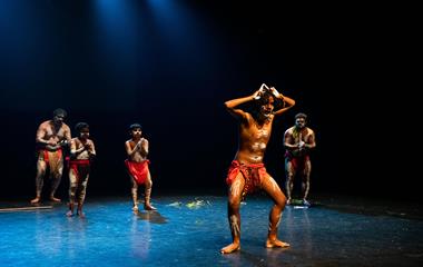 Five males wearing traditional attire during a cultural performance on stage.