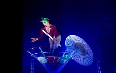 A performer on stage standing in a large martini glass wearing a red body suit.