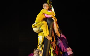 A group of performers dancing on stage with various objects.