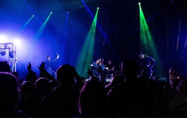 Three female artists wearing masks and performing on stage.