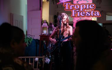 A female artist singing and playing the guitar to a crowd.