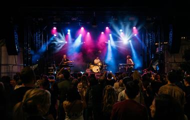 Three artists on stage with microphones and instruments performing to a crowd.