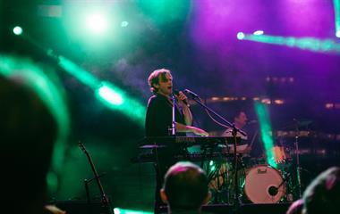 A male artist on stage with a microphone and a keyboard.