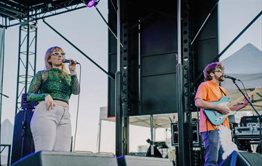 Two artists singing on stage with microphones and a guitar.