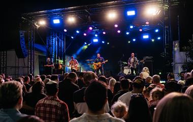 Three artists on stage with microphones and instruments performing to a crowd.