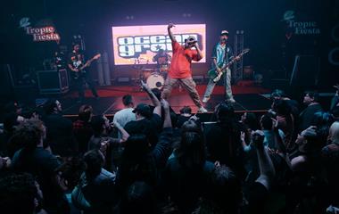 Four male artists on stage with microphones and musical instruments performing to a crowd.