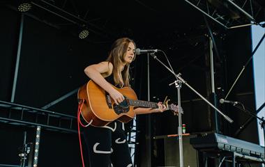 alt=" Female musican playing the guitar"