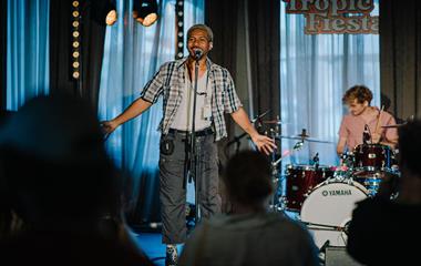 A male artist on stage with a microphone and a man playing the drums.