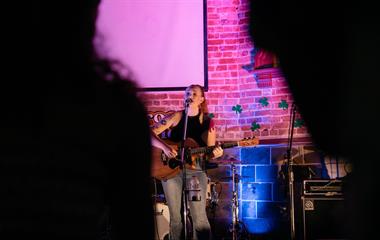 A female artist on stage with a microphone holding a guitar.