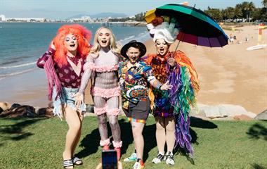 A group of people wearing colourful clothes and an umbrella posing for a photo.