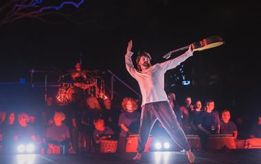 A man on stage holding a guitar with one hand.