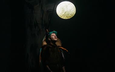 A man wearing a beetle costume while looking up at a circular light.