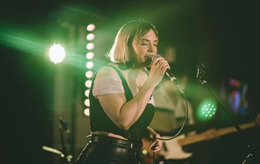 A female artist on stage singing into a microphone.
