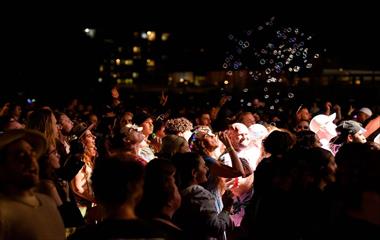 A crowd of people with a woman blowing bubbles into the air.